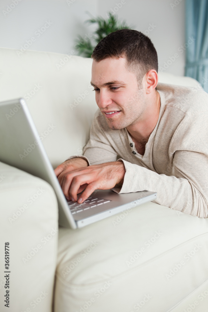 Portrait of a smiling man lying on a couch using a laptop Portrait of a smiling man lying on a couch using a laptop