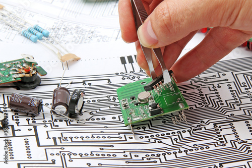 A hand hand with tweezers holding a electronic circuit board on