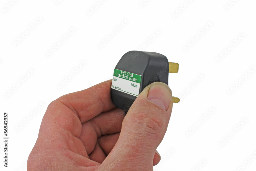 isolated hand on uk plug with blank pat test sticker