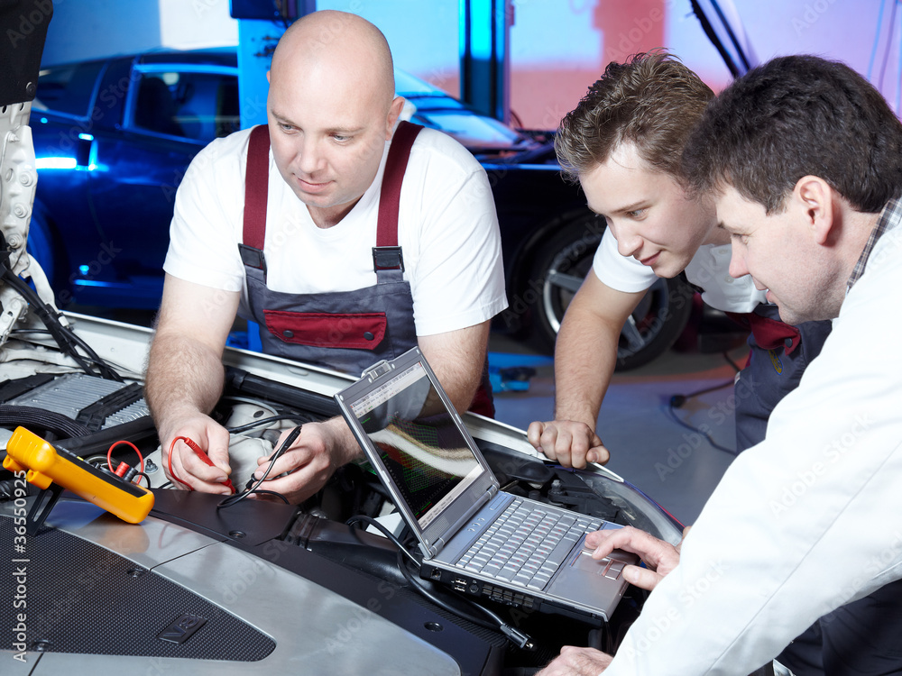 Three motor mechanics tuning the engine of a car in a garage Three motor mechanics tuning the engine of a car in a garage
