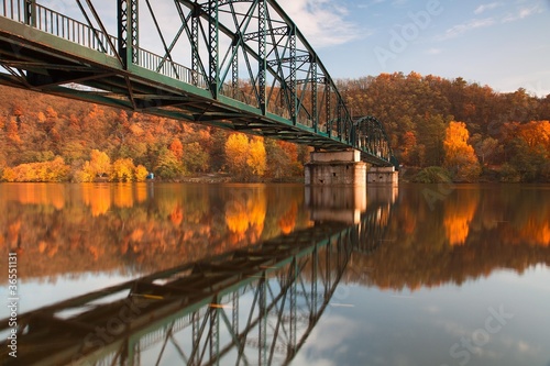 Fototapeta Naklejka Na Ścianę i Meble -  Metal bridge connecting river banks with reflection in autumn