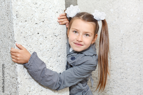 Little girl in grey coat looking from the wall