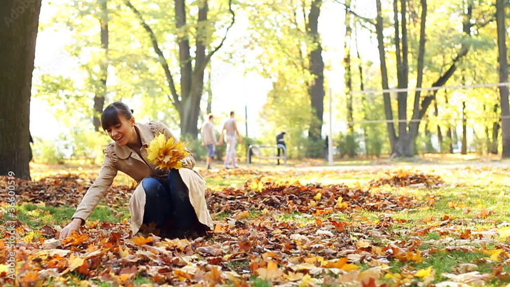 woman picking up golden leaves in autumn park, slow motion