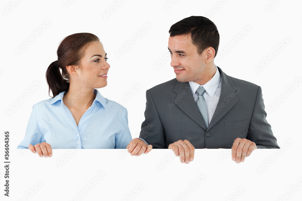 Business partners looking at each other while holding sign toget Business partners looking at each other while holding sign toget