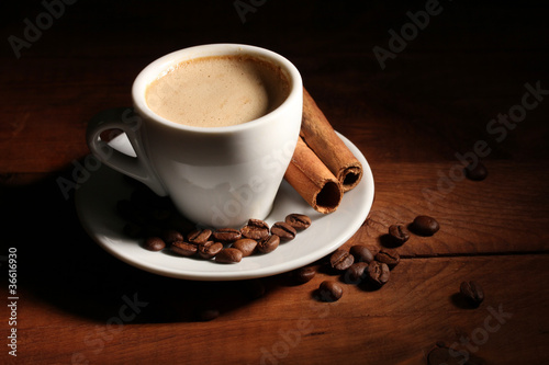 cup with coffee, cinnamon and coffee beans on wooden table