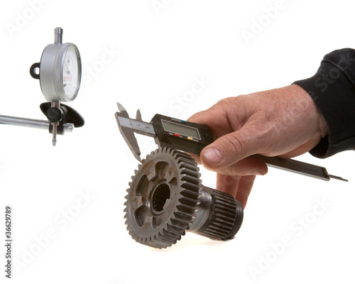 Measuring gearwheel with calipers with dial gauge in background.