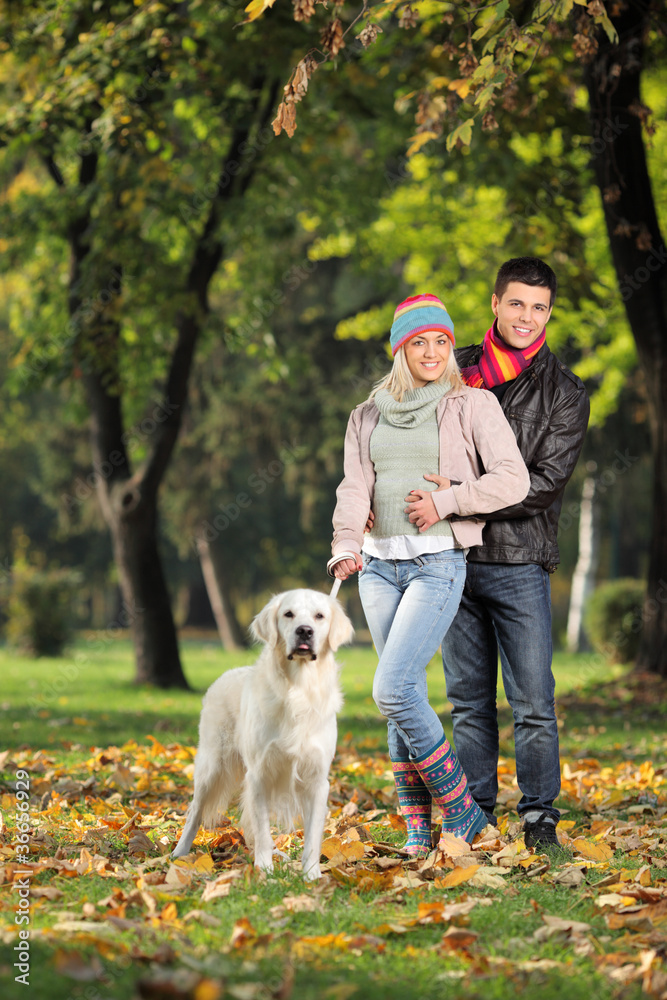 A smiling couple and their dog posing in the park