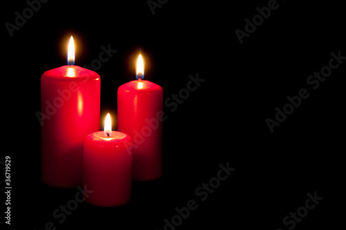 Set of three red candles burning in the dark