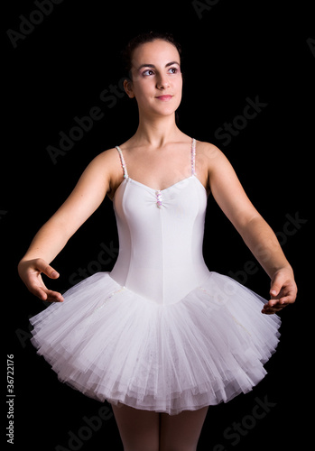 Teen girl ballet dancer standing in a tutu on a black background
