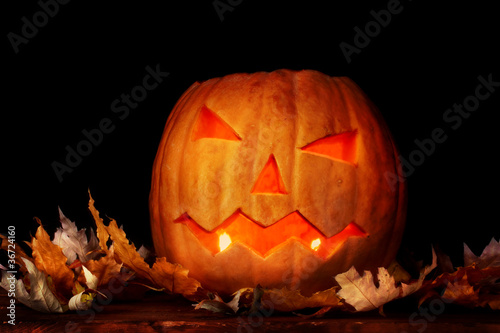 Halloween Pumpkin and autumn leaves on wooden table in dark