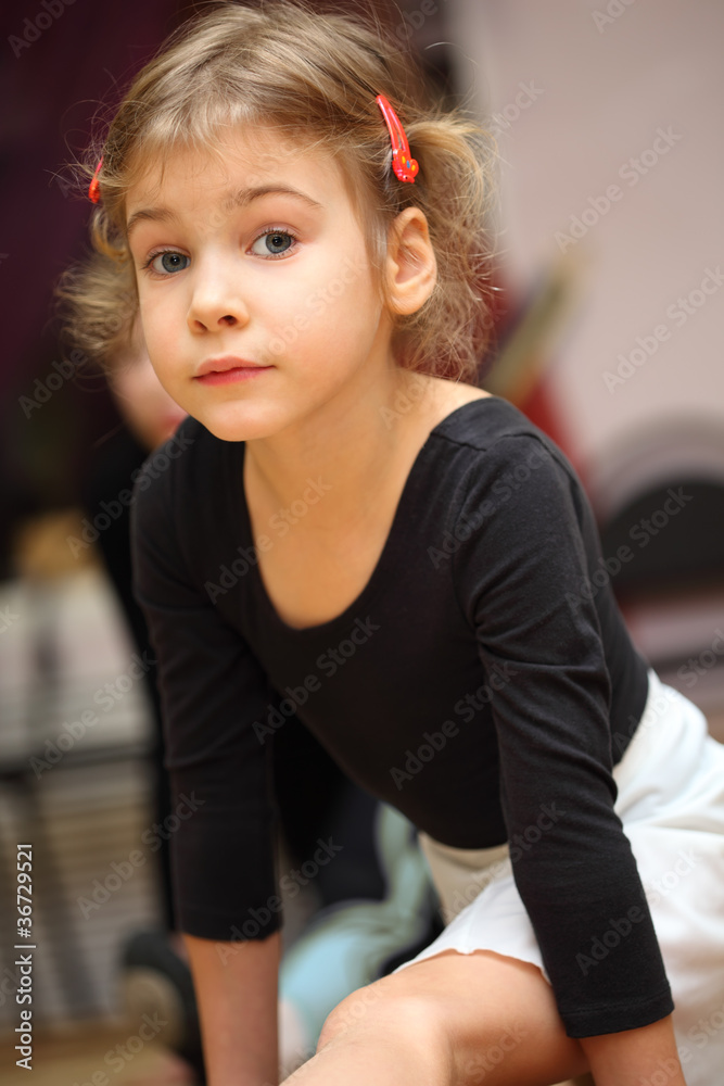 little girl in ballet class sits on string on floor and looks Stock