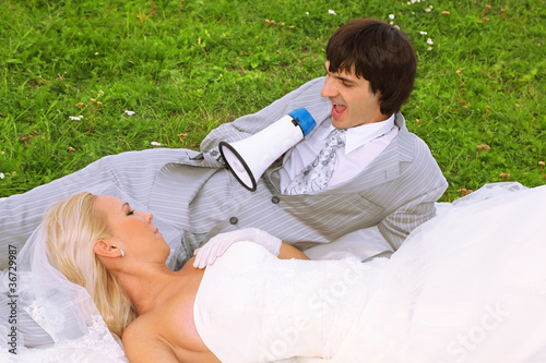 Beautiful young groom and bride wearing white dress lie on grass photo