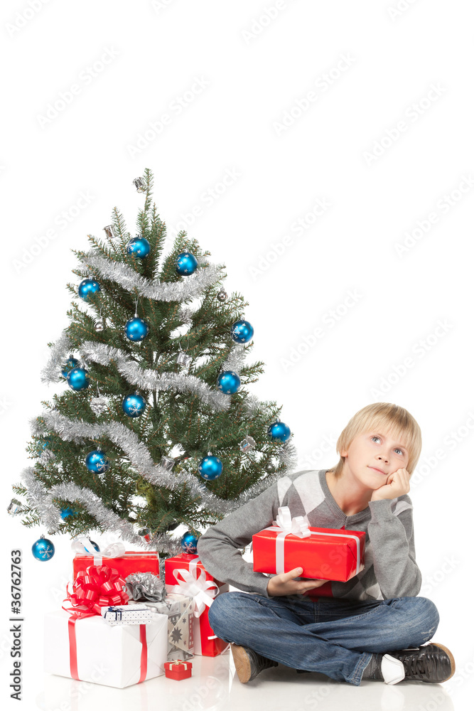 Pensive boy sitting near Christmas tree on the floor Pensive boy sitting near Christmas tree on the floor