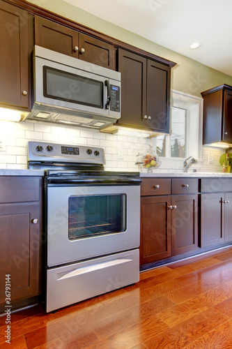 Modern new brown kitchen stove and microwave with cherry floor.