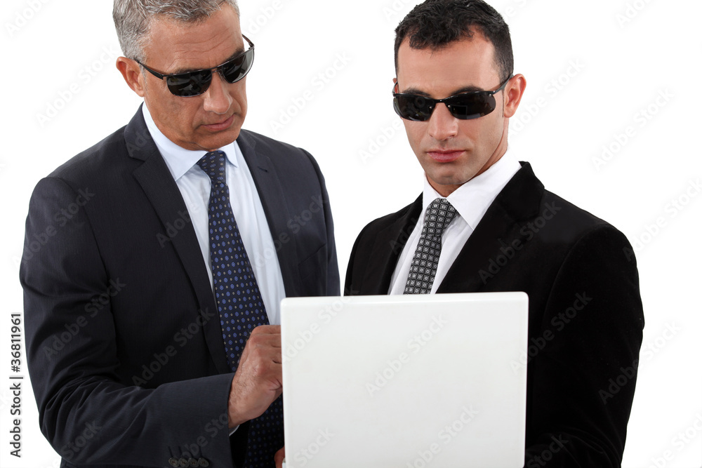 Serious men in smart suits with sunglasses holding a laptop Serious men in smart suits with sunglasses holding a laptop