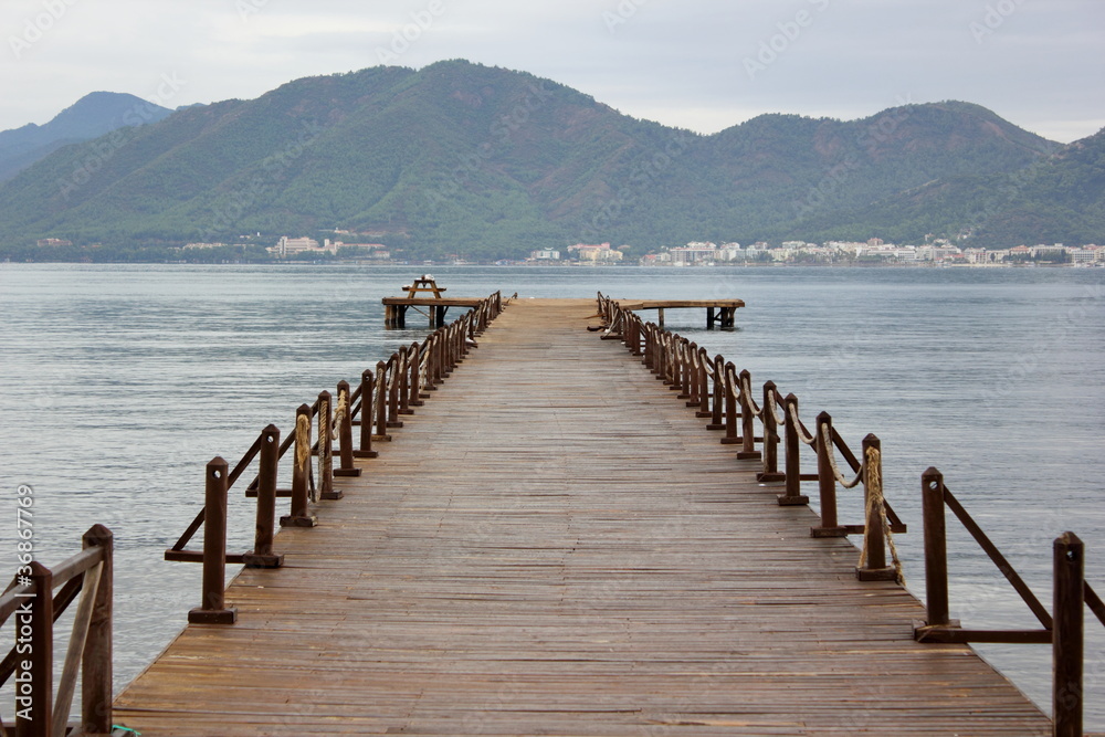 Wooden Pier over calm water of the sea to the mountains