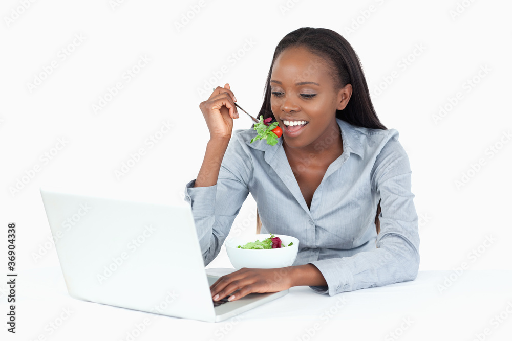 Businesswoman working with a laptop while eating a salad Businesswoman working with a laptop while eating a salad