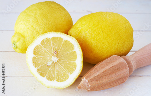 Closeup of three lemons and lemon juicer on white