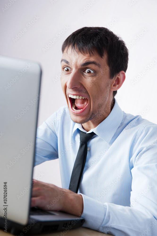 Attractive young man working with a laptop at his office. He is Attractive young man working with a laptop at his office. He is