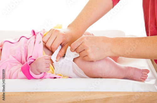 Mother changing little girl's diaper on nursery table