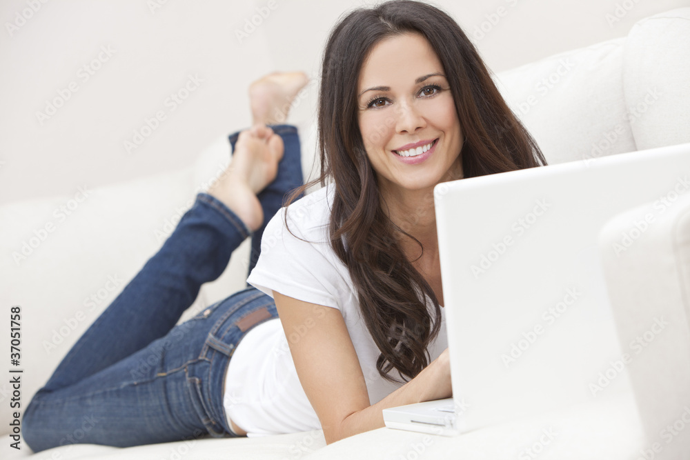 Young Brunette Woman Using Laptop Computer At Home on Sofa Young Brunette Woman Using Laptop Computer At Home on Sofa