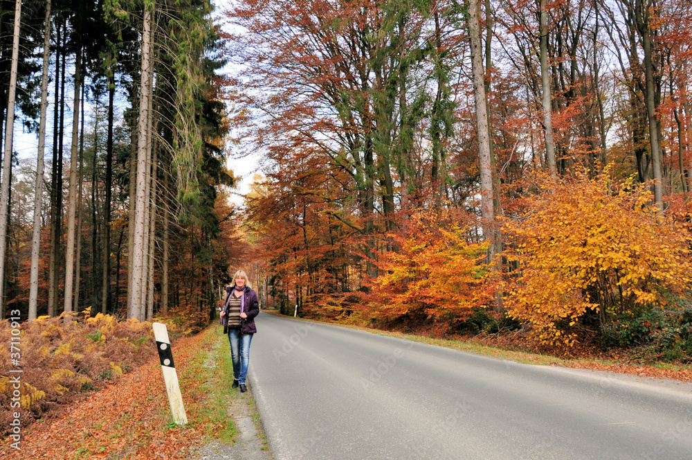 Fußgängerin an der Straße im Herbstwald Fußgängerin an der Straße im Herbstwald