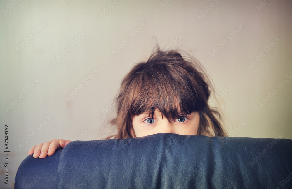 Fototapeta premium Little girl playing hide and seek behind the sofa