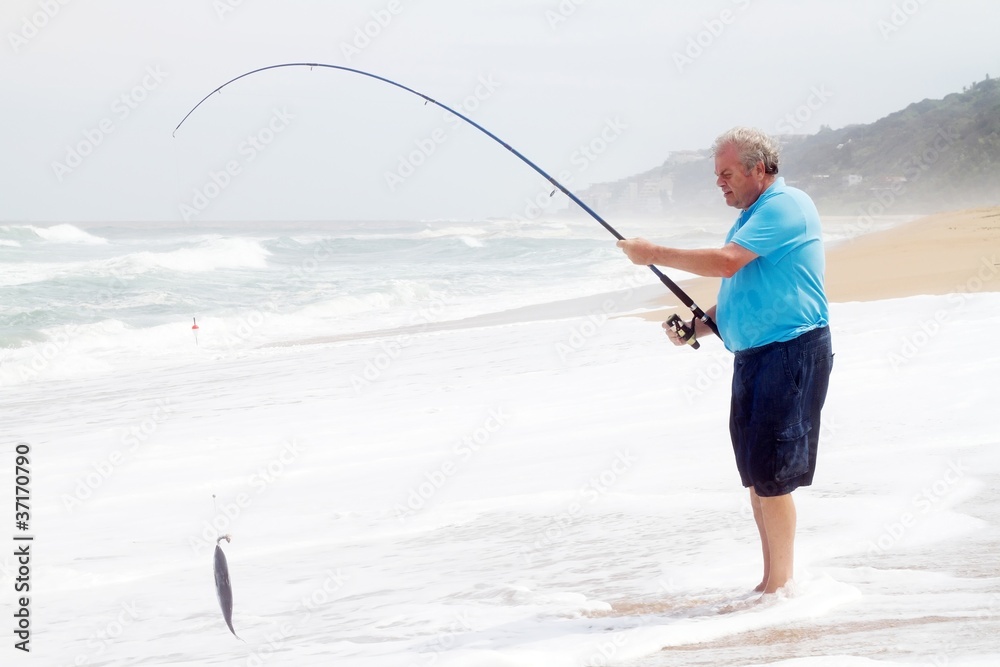 senior man catching a fish with fishing rod on beach senior man catching a fish with fishing rod on beach