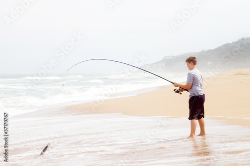 teen boy pulling a fish out of water with fishing rod