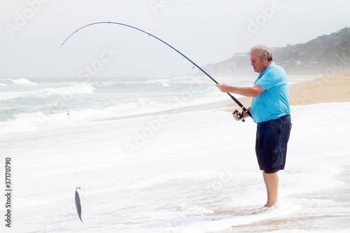 senior man catching a fish with fishing rod on beach