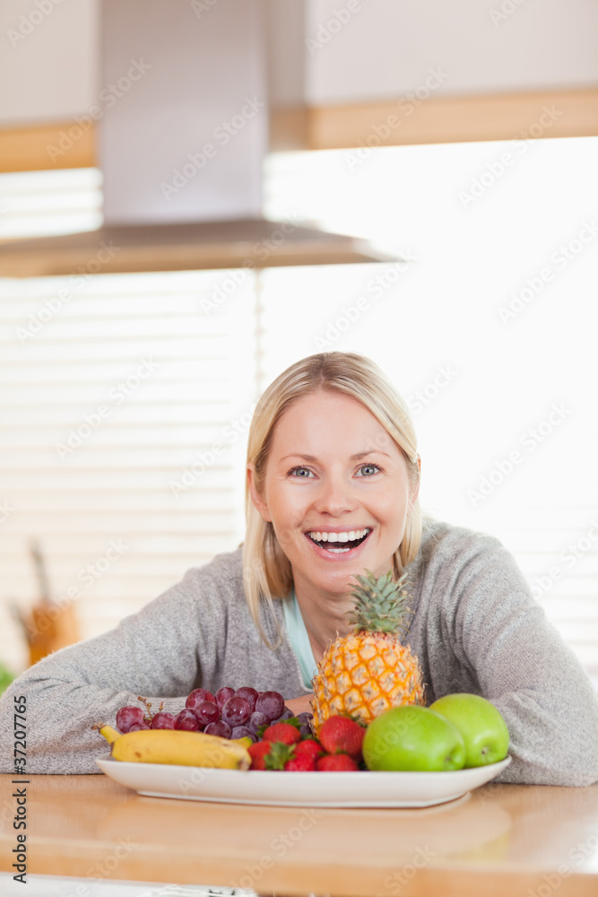 Laughing woman sitting behind plate of fruits Laughing woman sitting behind plate of fruits