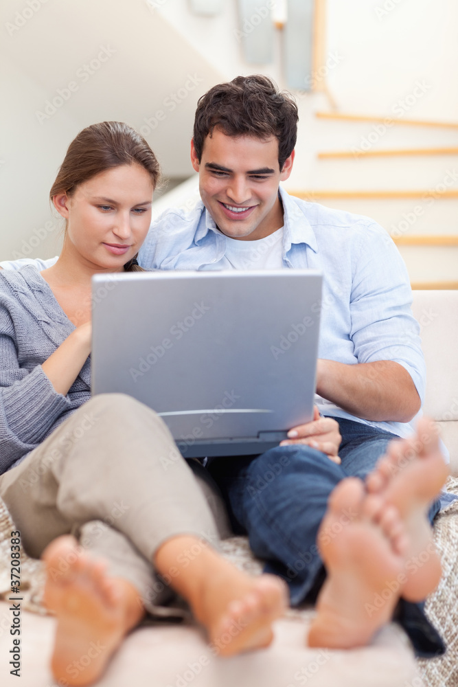 Portrait of a couple using a laptop while lying on a couch Portrait of a couple using a laptop while lying on a couch