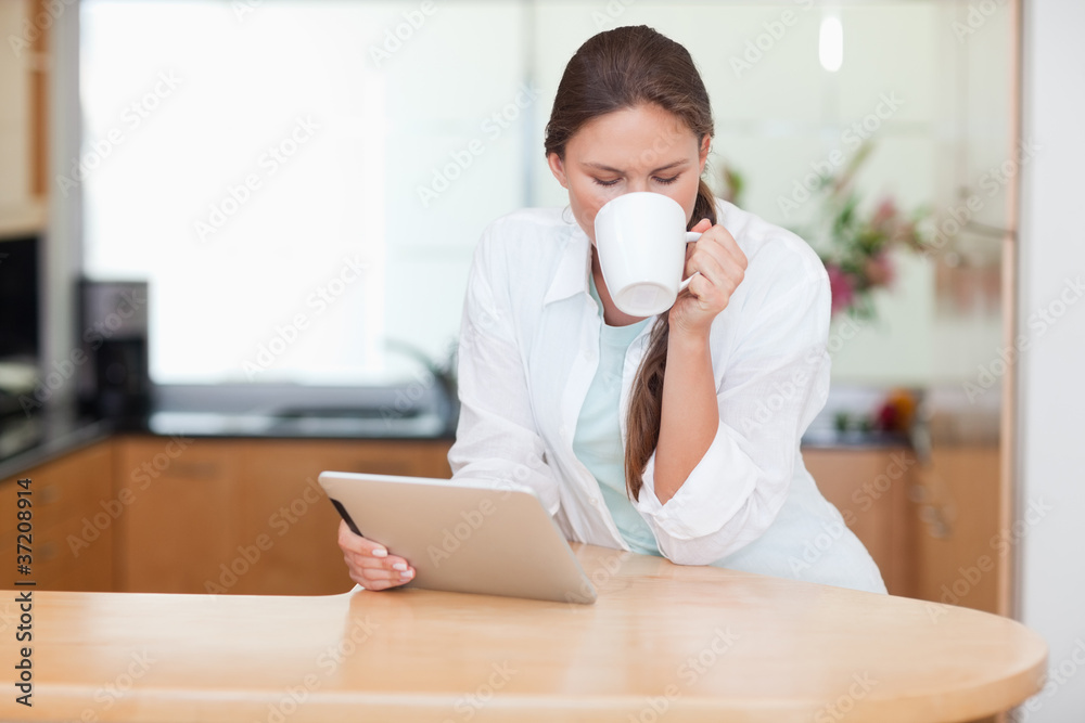 Woman using a tablet computer while drinking coffee Woman using a tablet computer while drinking coffee