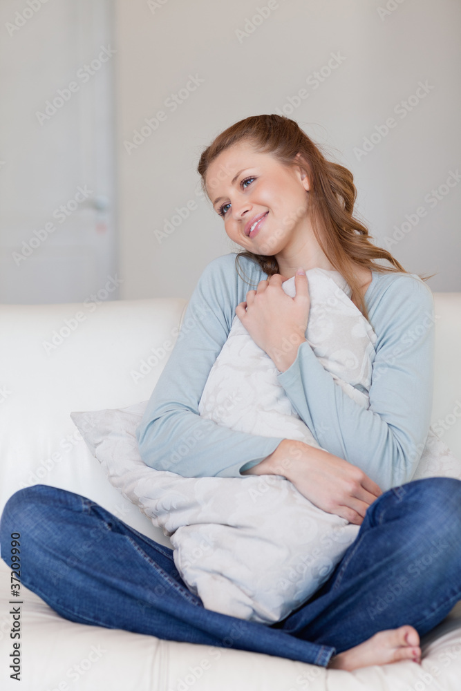 Smiling female sitting on the sofa embracing a pillow Smiling female sitting on the sofa embracing a pillow