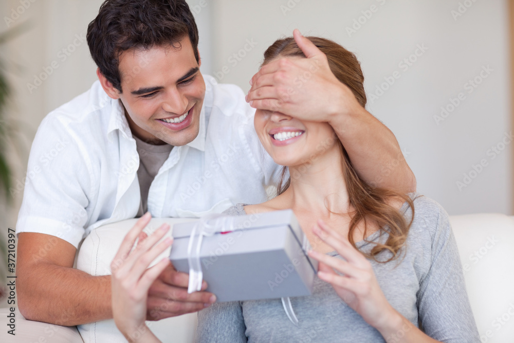 Man covering the eyes of his girlfriend while giving her a prese Man covering the eyes of his girlfriend while giving her a prese
