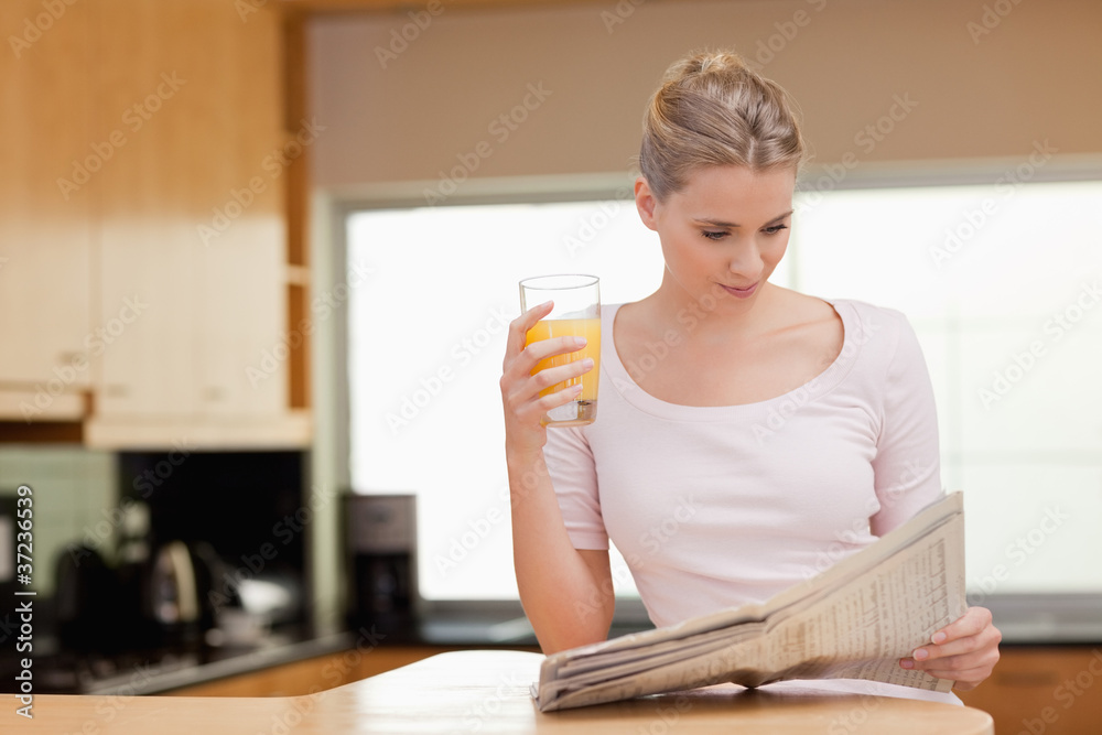 Woman reading the news while drinking orange juice Woman reading the news while drinking orange juice