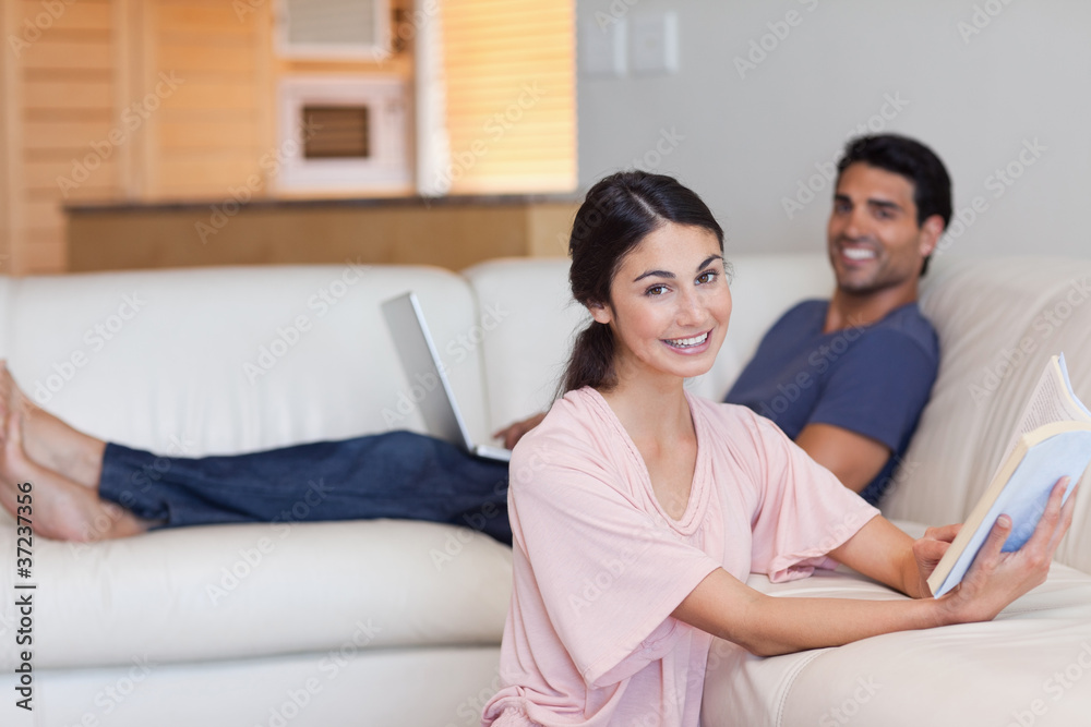 Woman reading a book while her boyfriend is using a laptop Woman reading a book while her boyfriend is using a laptop