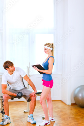Young man lifting a dumbbell under the supervision of trainer
