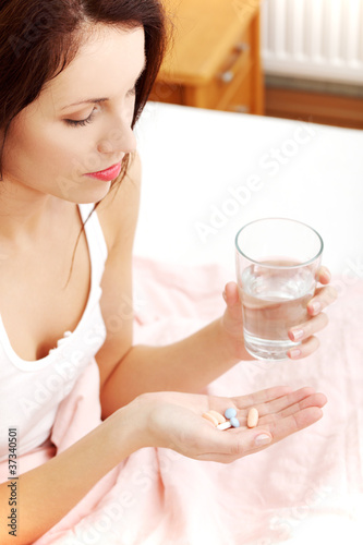 Beautiful woman holding pills and a glass of water.