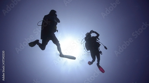 Silhouette view of two adult scuba divers.
