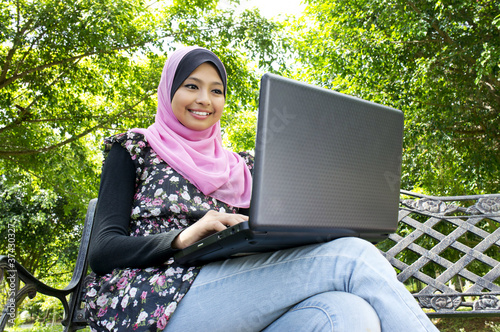 Beautiful Muslim girl sitting on bench with notebook
