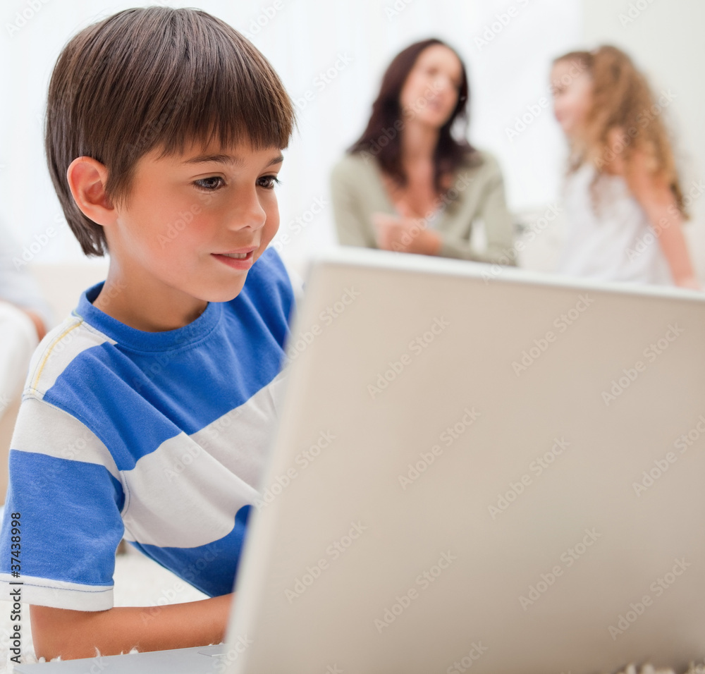 Boy playing computer games with his family behind him Boy playing computer games with his family behind him