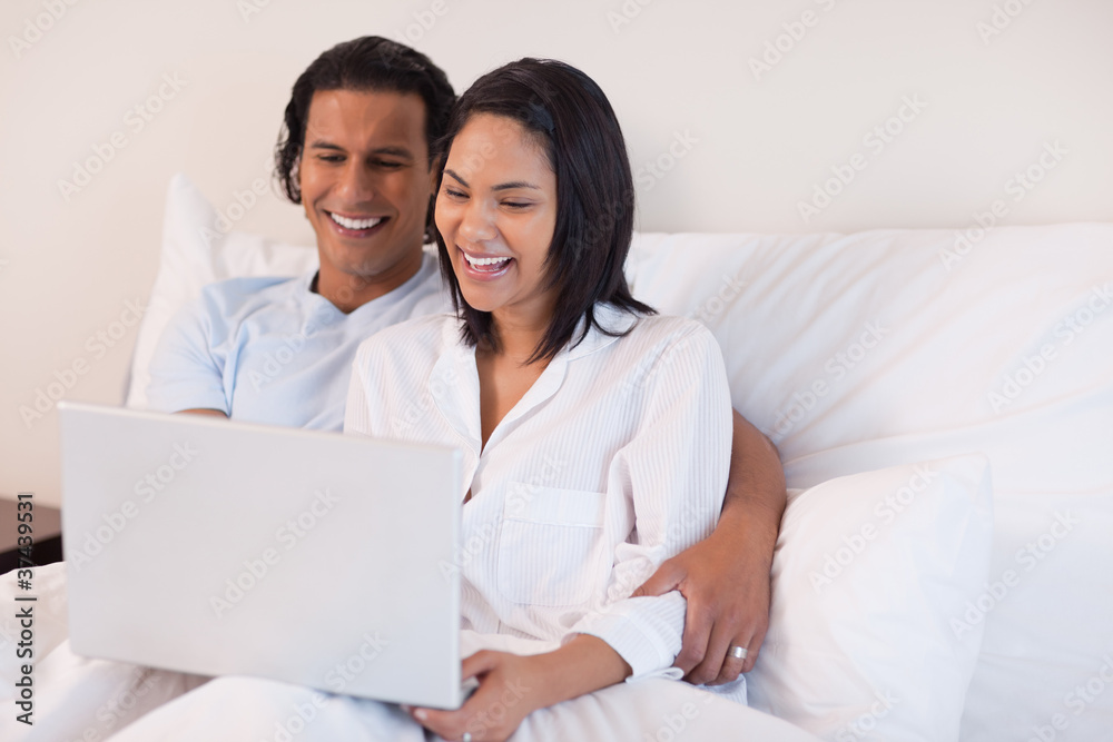 Couple using their laptop while sitting on the bed Couple using their laptop while sitting on the bed