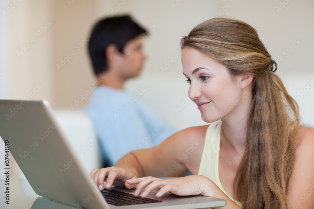 Woman using a laptop while her fiance is sitting on a couch