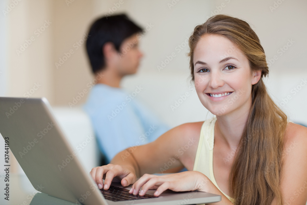 Woman using a notebook while her fiance is sitting on a sofa Woman using a notebook while her fiance is sitting on a sofa