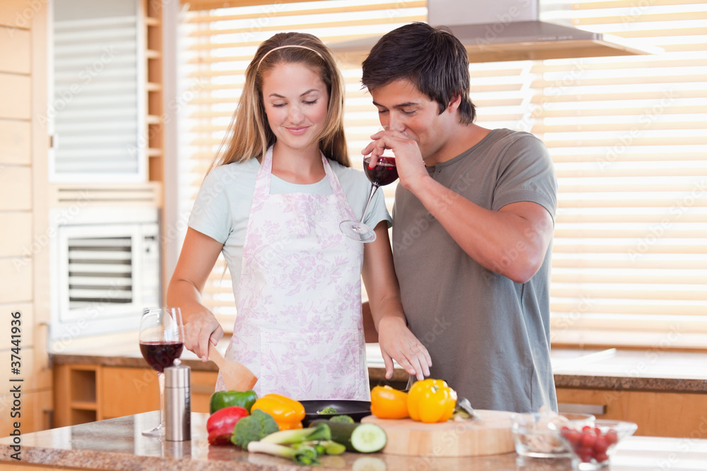 Young couple cooking dinner while drinking red wine