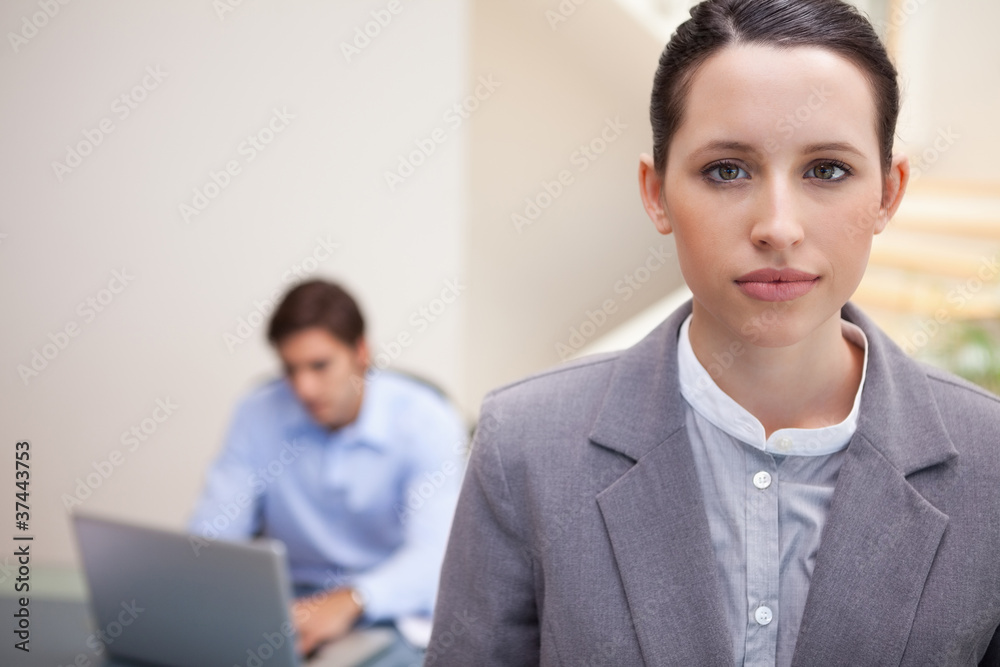 Businesswoman with colleague on his laptop behind her Businesswoman with colleague on his laptop behind her