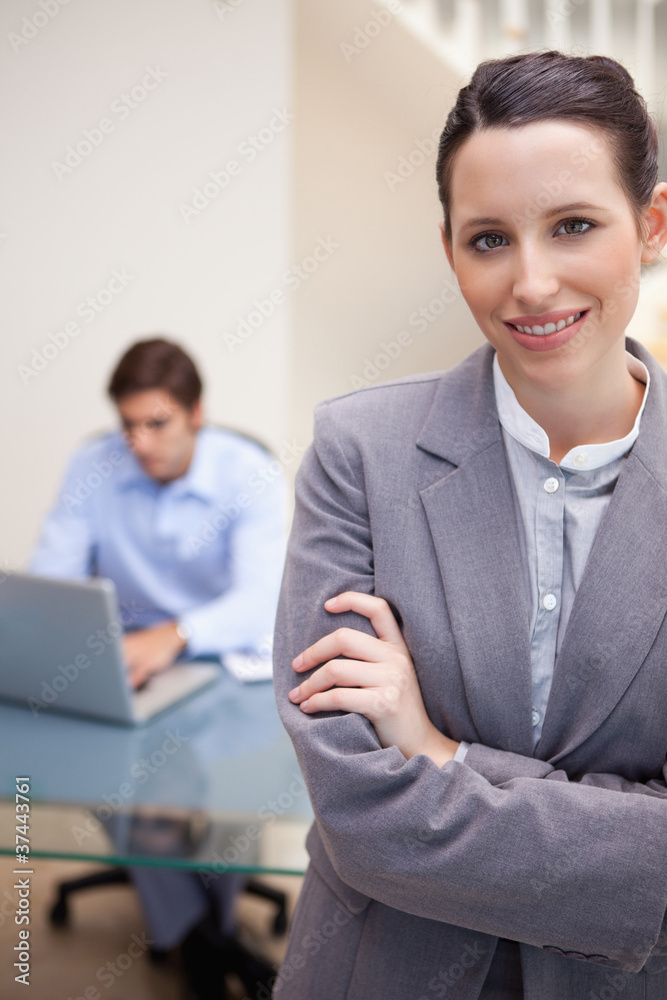 Smiling businesswoman with colleague on his laptop behind her Smiling businesswoman with colleague on his laptop behind her