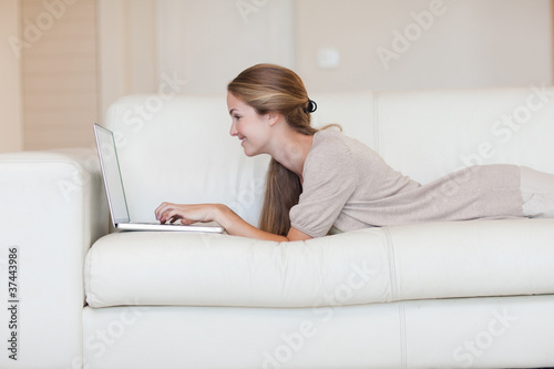 Side view of woman lying on the couch working on her laptop