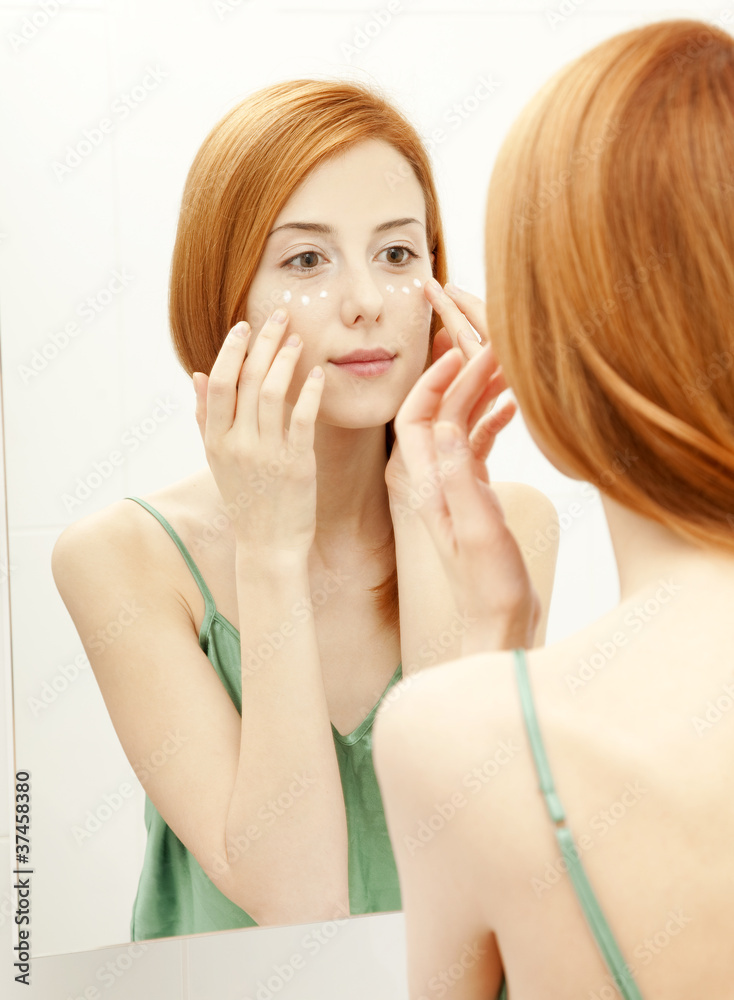 Beautiful redhead young woman with cream on the face in bathroom Beautiful redhead young woman with cream on the face in bathroom